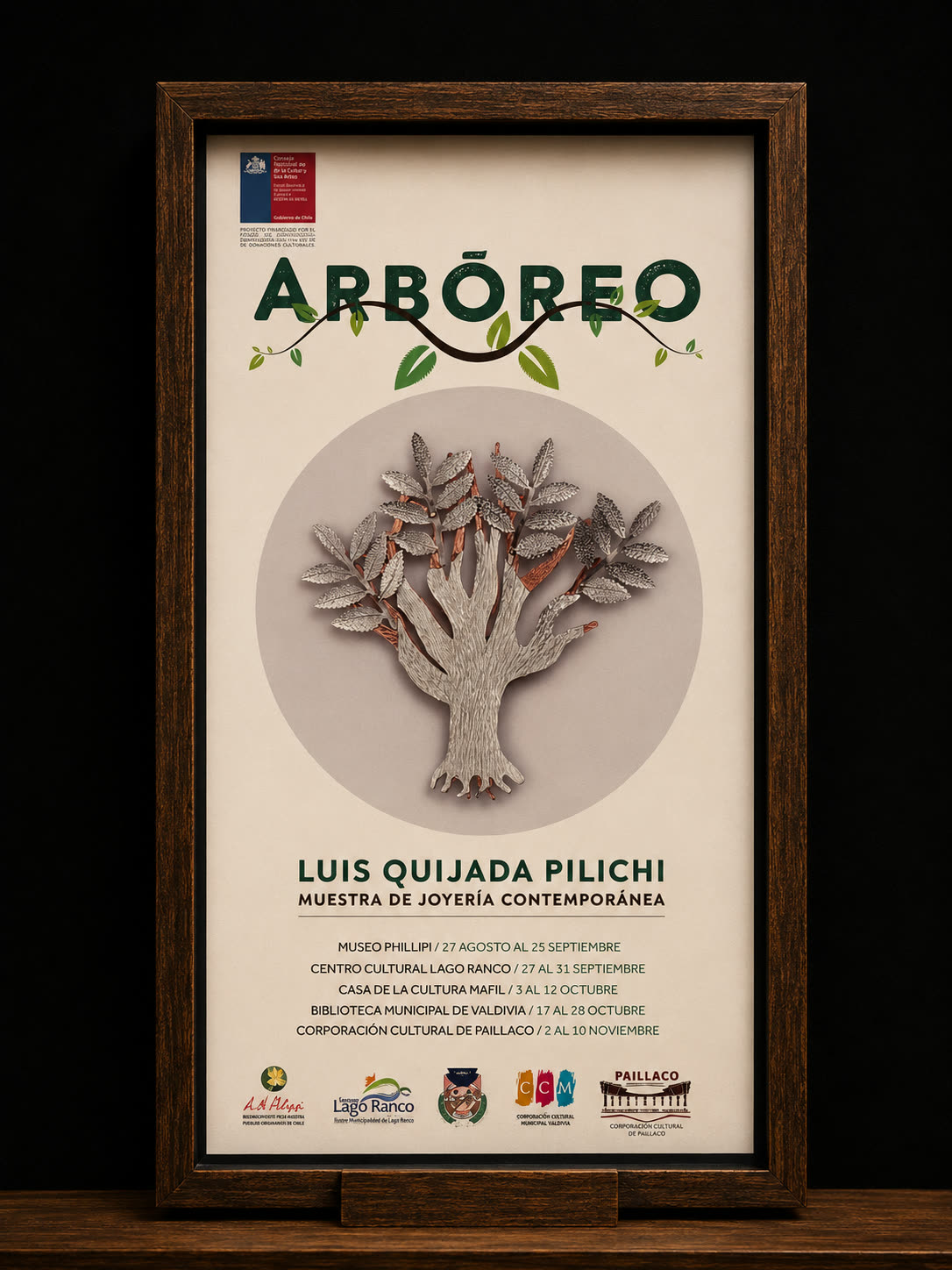Afiche enmarcado de la muestra Arbóreo: un árbol de plata y cobre sobre fondo claro, con el listado de sedes.